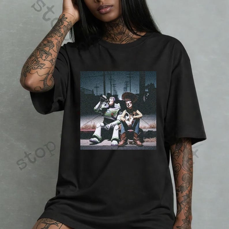 Puede incluir: Camiseta negra con un gr&aacute;fico de Buzz Lightyear y Woody de Toy Story sentados juntos. La imagen es un dise&ntilde;o estilizado de estilo vintage con un fondo oscuro y urbano.