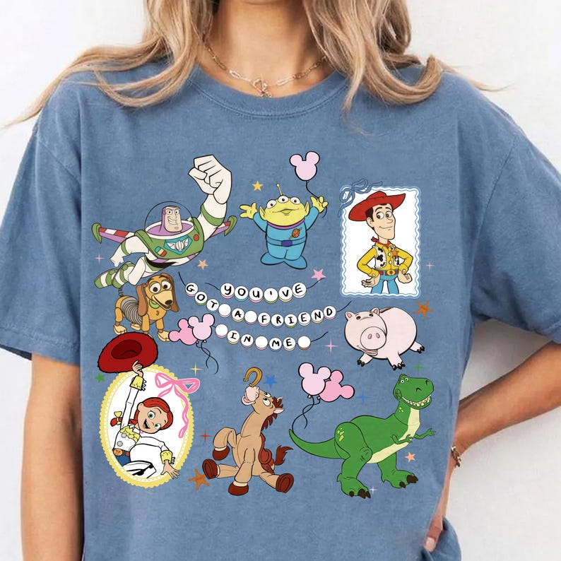May include: A blue t-shirt featuring a graphic print of Toy Story characters including Buzz Lightyear, Woody, Jessie, Slinky Dog, Rex, Hamm, and an Alien. The text "YOU'VE GOT A FRIEND IN ME" is displayed in the center with small star and balloon accents.