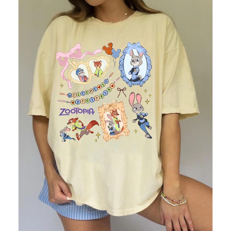 May include: A light yellow t-shirt featuring various cartoon images and the word "Zootopia". The shirt has a crew neck and short sleeves. The graphics include framed character portraits and decorative elements.