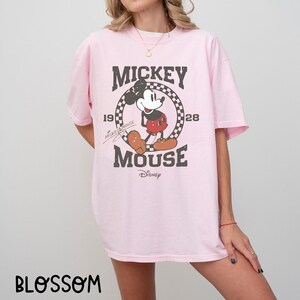 Peut inclure: T-shirt rose clair avec un motif vintage de Mickey Mouse. Le design comprend les mots "Mickey Mouse" et "Disney" avec l'ann&eacute;e "1928". Le t-shirt a des manches courtes et une coupe ample.