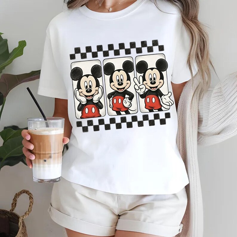 May include: White t-shirt featuring a graphic of Mickey Mouse in three different poses. The design includes a black and white checkered border. Mickey is wearing his signature red shorts and black gloves.