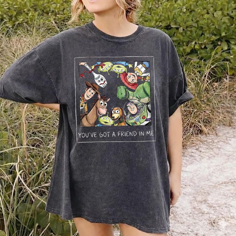 K&ouml;nnte beinhalten: Dunkelgraues T-Shirt mit einer farbenfrohen Grafik von Figuren aus dem Film Toy Story. Die Grafik ist in einem wei&szlig;en Rechteck gerahmt und enth&auml;lt den Text "YOU'VE GOT A FRIEND IN ME". Das Shirt hat kurze &Auml;rmel und eine lockere Passform.