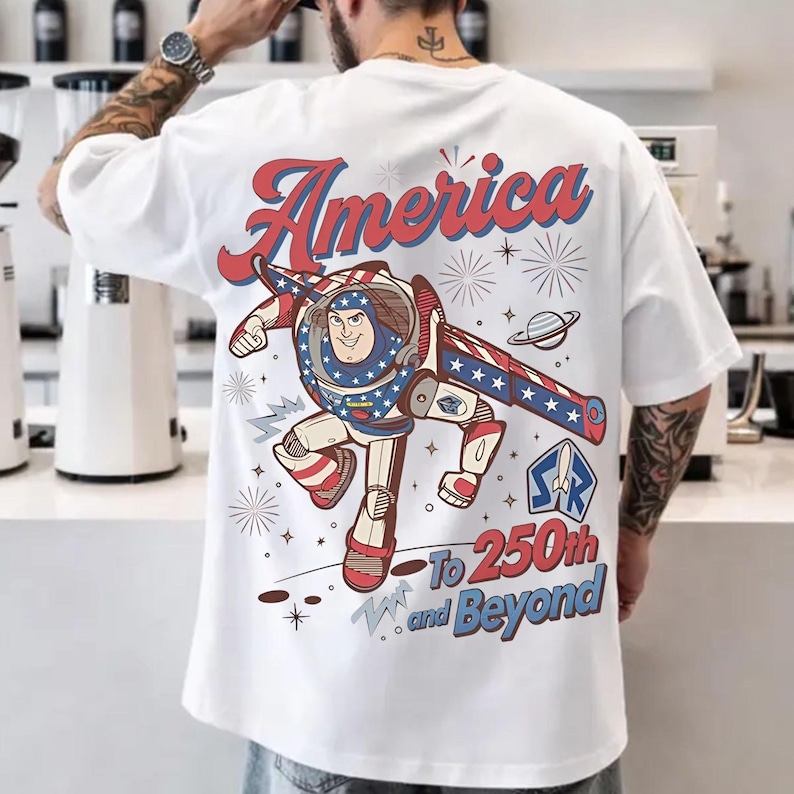 May include: A white t-shirt featuring a graphic of a space ranger character in a red, white, and blue suit. The text reads America To 250th and Beyond, accompanied by illustrations of stars, fireworks, a planet, and a rocket ship emblem.