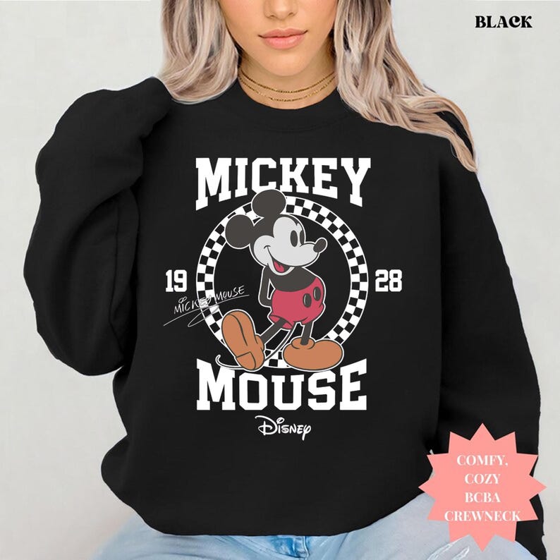 Peut inclure: Sweat-shirt noir &agrave; col rond avec un motif Mickey Mouse. Le design comprend le mot "Mickey" au-dessus d'un motif en damier circulaire avec "1928" de chaque c&ocirc;t&eacute;. Le logo Disney est en bas. Le mot "BLACK" est en haut.