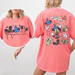 K&ouml;nnte beinhalten: Korallfarbenes T-Shirt mit Mickey Mouse-Motiven. Auf der Vorderseite sind Mickey Mouse-Ohren, ein Zaubererhut und Text abgebildet. Auf der R&uuml;ckseite ist Mickey als Zauberer zu sehen, zusammen mit anderen Grafiken. Das Shirt ist ein l&auml;ssiger, bequemer Stil.