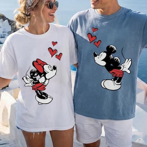 May include: White and blue t-shirts featuring Mickey and Minnie Mouse designs. The Mickey Mouse design is on a blue shirt, and the Minnie Mouse design is on a white shirt. Both designs include red hearts.
