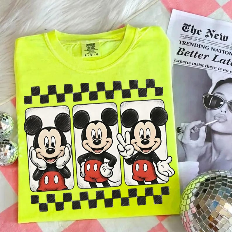 May include: Neon yellow t-shirt featuring three panels with Mickey Mouse illustrations. Each panel showcases a different pose of Mickey Mouse, with a black and white checkered border. The shirt has a crew neck and short sleeves.