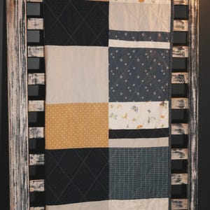 May include: A patchwork quilt featuring diverse fabric patterns, such as navy blue diamond, cream, and mustard yellow polka dots. The quilt is displayed on a distressed white wooden rack, highlighting its handcrafted design and colour palette.