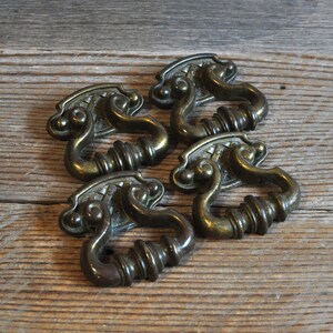 May include: Five antique brass cabinet drawer pulls with ornate designs. Each pull has a loop handle and a decorative backplate.