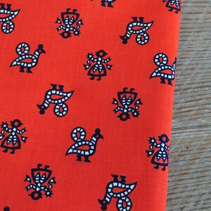 May include: Red fabric with a repeating pattern of black and white stylized figures. The figures include birds, flowers, and geometric shapes.