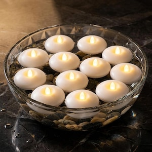 May include: A clear glass bowl filled with water, small stones, and white floating candles. Each candle has a warm, yellow glow, creating a soft, ambient light. The bowl sits on a dark, marbled surface.