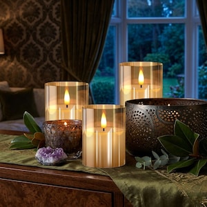 May include: A collection of decorative candles in glass holders and a dark metal bowl. The candles have a warm, inviting glow, with a flickering flame effect. The arrangement includes a purple amethyst crystal and greenery on a green runner.