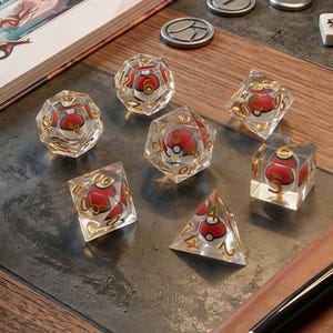 May include: A set of seven polyhedral dice made of clear resin, each containing a miniature red and white spherical object inside. The dice feature gold-colored numbers etched into the surfaces, including d20, d12, d10, d8, d6, and d4 shapes.
