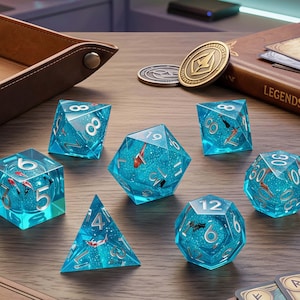 May include: A set of clear blue polyhedral dice with koi fish and silver numbering. The dice are arranged on a wooden table with a leather tray, coins, and a book titled "LEGENDS".