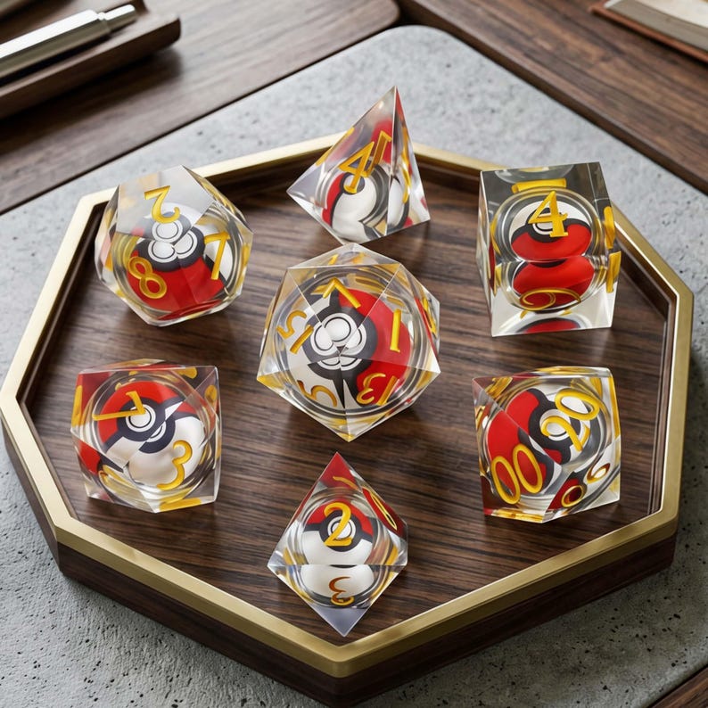 May include: A set of seven clear polyhedral dice, each containing a miniature red, white, and black spherical design inside. The dice feature gold-colored numbers etched into the transparent surfaces, arranged on a wooden hexagonal tray.