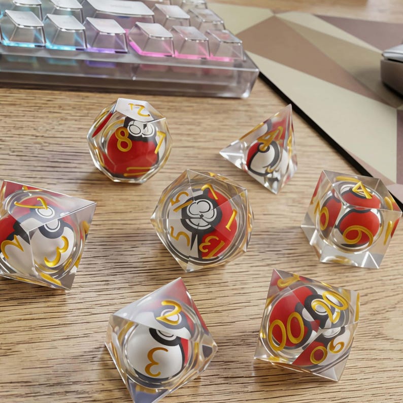 May include: A set of seven polyhedral dice made of clear resin, each containing a miniature red, white, and black spherical object resembling a ball. The dice feature gold-colored numbers etched into the transparent surfaces for game play.