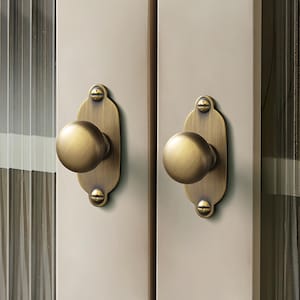 Op de afbeelding: Detailopname van twee kastdeuren met messingkleurige knoppen en achterplaten. De deuren zijn neutraal van kleur en de glazen panelen hebben verticale, getextureerde lijnen. De knoppen zijn rond.