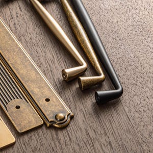 May include: Close-up of various cabinet hardware in antique brass, gold, and black finishes. The selection includes pull handles and rectangular backplates, showcasing different styles and designs for home decor and renovation projects.