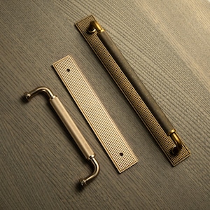 Op de afbeelding: Drie decoratieve deurgrepen en handgrepen in messing en bronzen tinten. De handgrepen hebben een getextureerde grip met een diamantpatroon. De rechthoekige achterplaten hebben ook een getextureerd oppervlak. De hardware is ontworpen voor kasten en deuren.