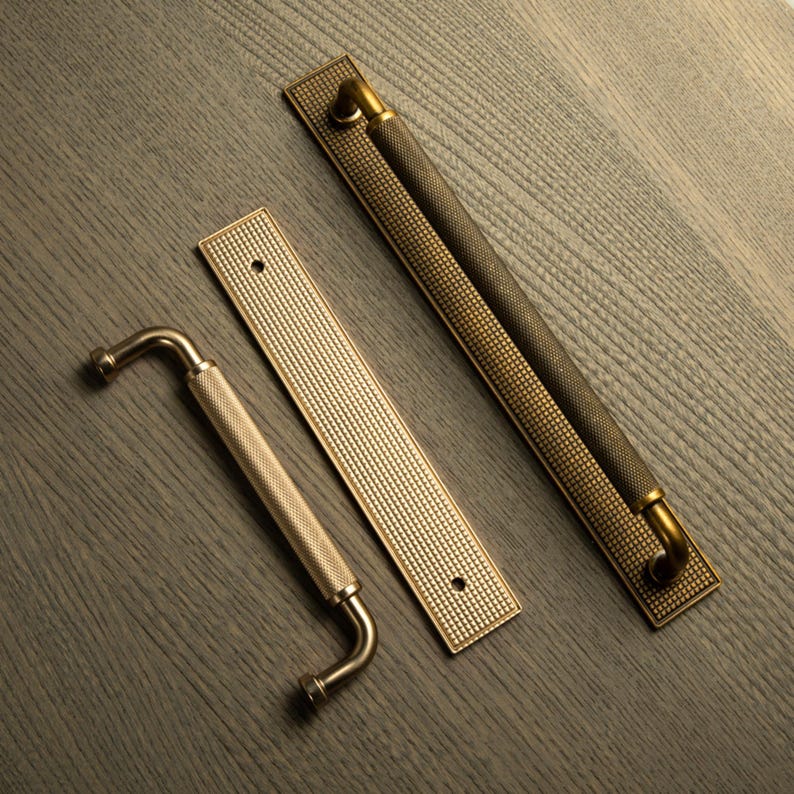 Op de afbeelding: Drie decoratieve deurgrepen en handgrepen in messing en bronzen tinten. De handgrepen hebben een getextureerde grip met een diamantpatroon. De rechthoekige achterplaten hebben ook een getextureerd oppervlak. De hardware is ontworpen voor kasten en deuren.