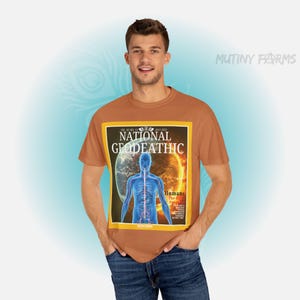 May include: A brown t-shirt featuring a parody of a magazine cover with the text "NATIONAL GEODEATHIC" and an illustration of a human figure and a planet. The shirt is worn by a person with blue jeans.