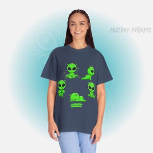 Op de afbeelding: Een marineblauw T-shirt met een ontwerp van groene cartoonaliens in verschillende poses. De aliens hebben grote ogen en bevinden zich in verschillende posities, waaronder zitten en liggen. De tekst "MUTINY FARMS" is zichtbaar.
