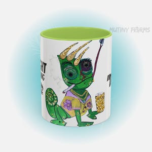 May include: White ceramic mug with a green interior featuring a cartoon chameleon with a cigarette, crown, and beer. The chameleon is green, yellow, and purple. The mug has the text "IGHT" and "MUTINY FARMS".