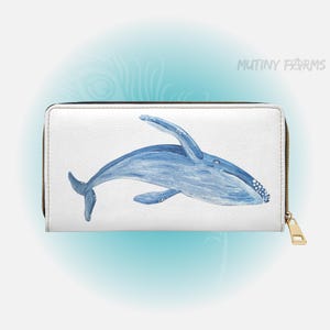 May include: White wallet featuring a blue whale illustration. The whale is painted in shades of blue with white accents. The wallet has a gold zipper and the text "MUTINY FARMS" is visible on the upper right.