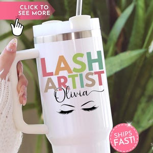 May include: White travel mug with a handle, featuring the text "LASH ARTIST Olivia" in colorful letters and a pair of stylized eyelashes. The mug has a silver rim and a white lid. A pink sticker says "SHIPS FAST!"