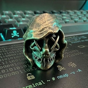 May include: A bronze-colored skull ring with a hooded design, resting on a keyboard with binary code and the text "root@terminal". The ring has intricate details and a menacing expression, perfect for a gothic or tech-inspired aesthetic.