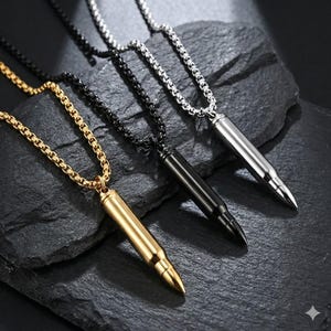 Könnte beinhalten: Drei Halsketten mit kugelartigen Anhängern in Gold, Schwarz und Silber. Jeder Anhänger hängt an einer passenden Kette. Die Halsketten werden auf einer dunklen, strukturierten Oberfläche präsentiert.