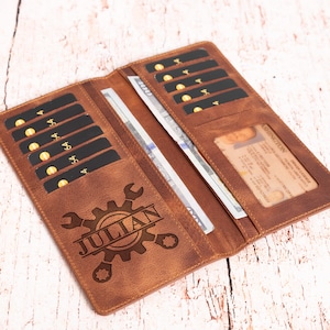 May include: Open brown leather wallet with multiple card slots, a clear ID window, and a cash compartment holding a stack of bills. The wallet is personalized with the name "JULIAN" and a gear and wrench design.