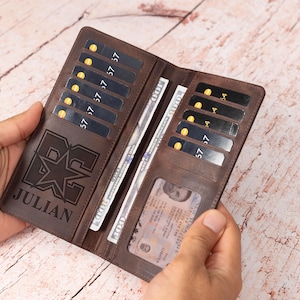 May include: A brown leather wallet with multiple card slots and a clear ID window. The wallet is open, revealing cash and cards. The name "JULIAN" is engraved on the front, along with a starburst design.