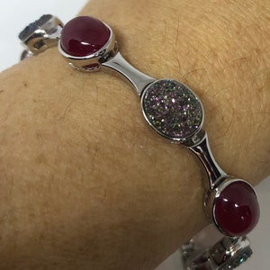 May include: A silver bracelet with three round red and iridescent stones. The bracelet is on a person's wrist.