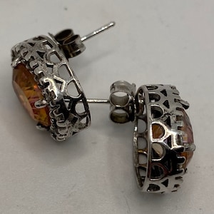 May include: A pair of silver earrings with a large, oval-shaped, orange and yellow gemstone set in a filigree design.