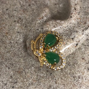 Op de afbeelding: Gouden vlinder oorbellen met groene edelsteen accenten en heldere kristallen versieringen.