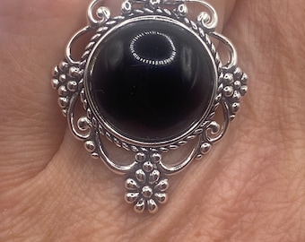 May include: A silver ring with a large black gemstone set in a decorative filigree design.