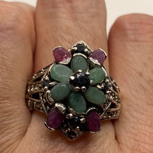 Op de afbeelding: Een zilveren ring met een bloemmotief met groene, roze en zwarte edelstenen.