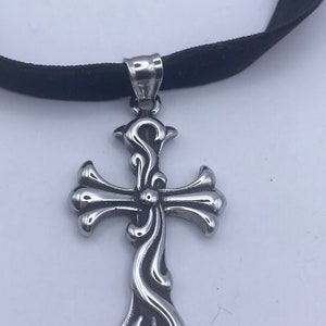 May include: A silver cross pendant with intricate details hangs from a black velvet choker.