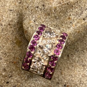May include: A silver ring with a band of small white diamonds and two rows of purple gemstones.