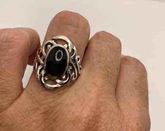 May include: A silver ring with an oval-shaped black stone set in a decorative filigree design.
