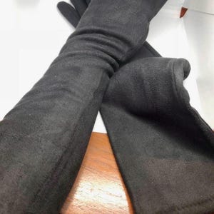 May include: A pair of long black gloves made of a soft, fuzzy material. The gloves are folded in half and the fingertips are visible.