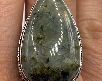 May include: A silver ring with a teardrop-shaped green and gray gemstone. The gemstone has a speckled pattern and is set in a silver bezel.