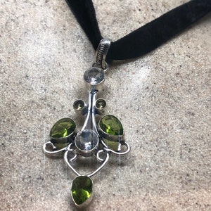 May include: A silver pendant necklace with a black velvet choker. The pendant features a delicate design with clear and green gemstones.