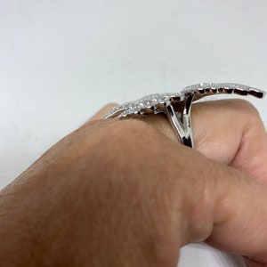 K&ouml;nnte beinhalten: Ein silberner Ring mit einem gro&szlig;en, komplizierten Design aus funkelnden Steinen. Der Ring wird an einem Finger getragen.
