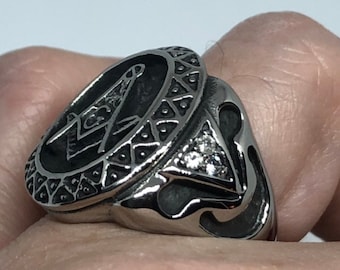 Könnte beinhalten: Ein silberner Ring mit einem schwarz-weißen Freimaurer-Symbol auf der Oberseite. Der Ring hat ein dekoratives Design um das Symbol herum und einen kleinen Diamanten an der Seite.