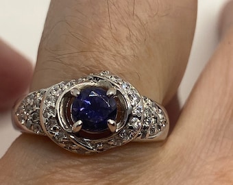 May include: A silver ring with a dark blue gemstone surrounded by smaller white gemstones.