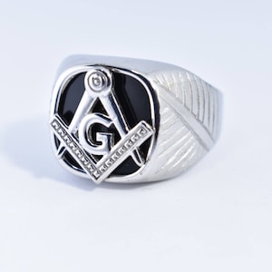 May include: A silver ring with a black onyx stone featuring a silver Masonic symbol.