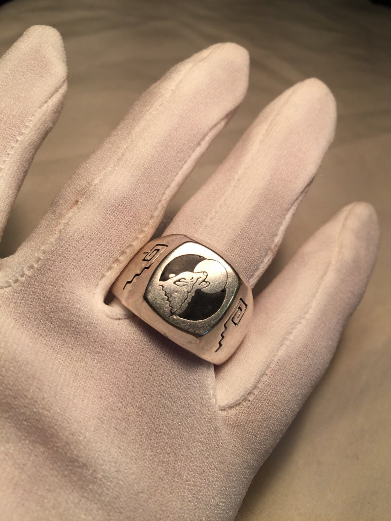 May include: A silver ring with a black and white design of a stylized animal head. The ring has a textured band with a wavy pattern.
