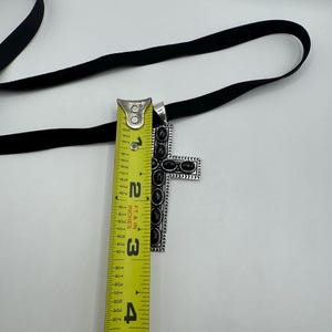 Op de afbeelding: Een zilveren kruis hanger met zwarte accenten en een zwart fluwelen lint van 7,6 cm lang.